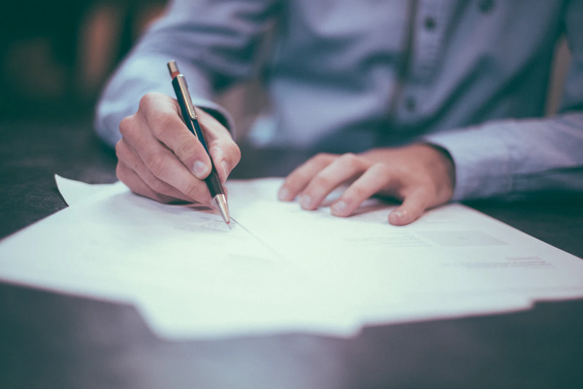 A hand signing a printed agreement at a desk